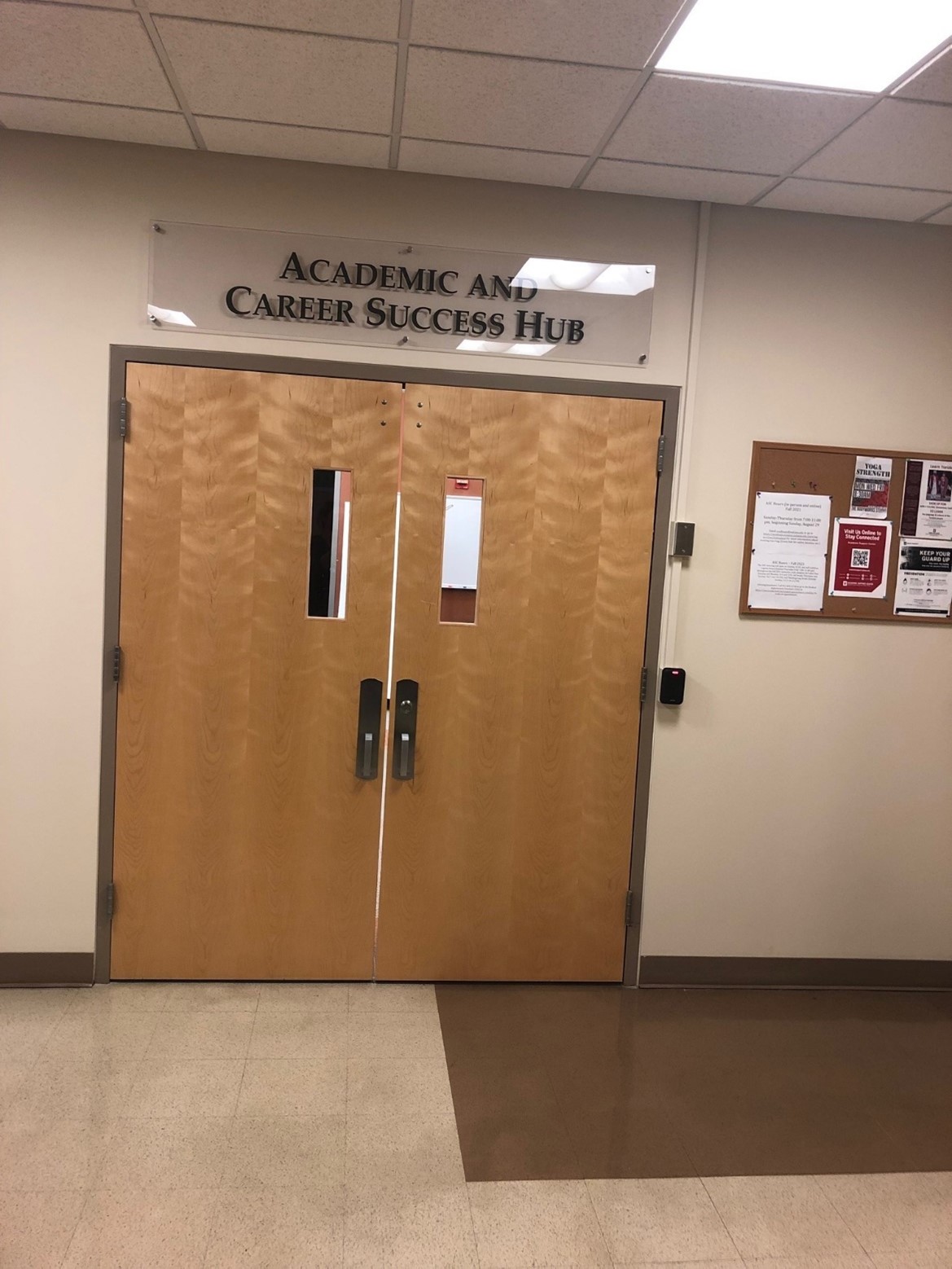A set of wooden double doors. There is a sign above the doors labeled "Academic and Career Success Hub" and a corkboard on the wall next to the doors.